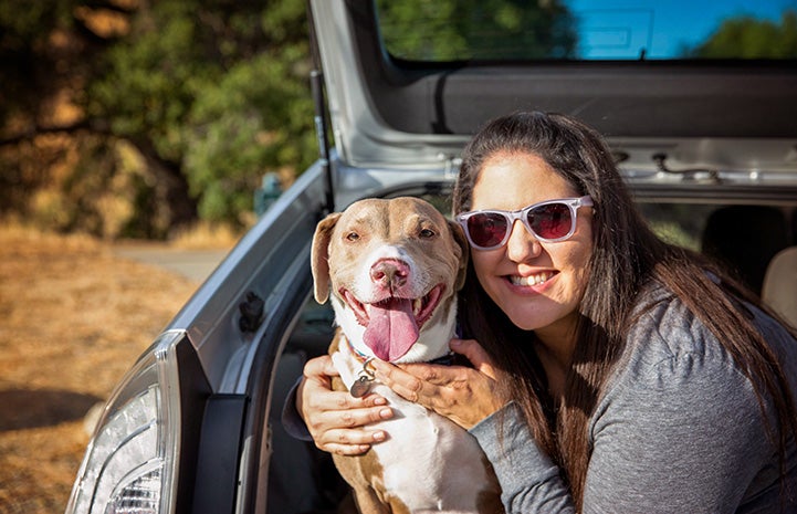 Woman hugging a brown and white dog from inside the back of a car's hatchback