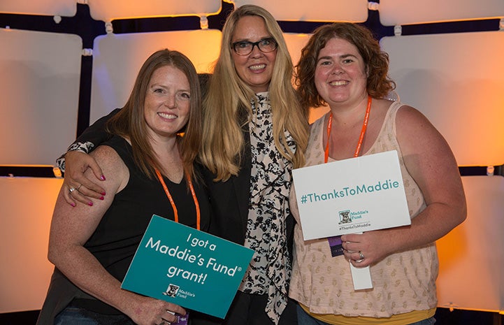 Julie Castle posing with two women holding signs at the Best Friends National Conference