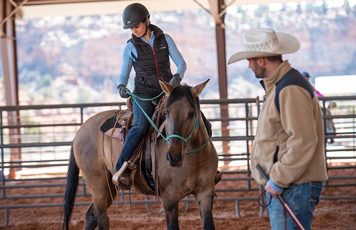 Woman holding the reins on a horse while a man in a cowboy hat watches