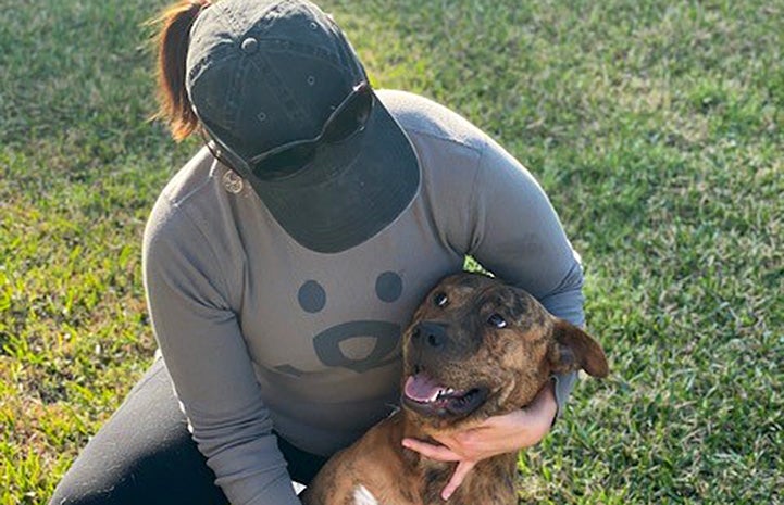 Person wearing hat and Best Friends shirt cradling Pancho the dog while out on the grass