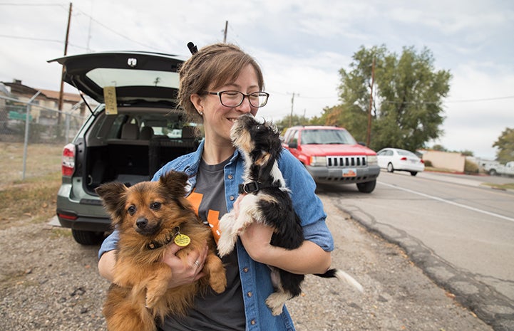 Smiling woman holding a fluffy brown dog and puppy who is kissing her face