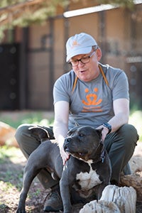 Volunteer Fred Rainey sitting next to Stitch, a black and white pit bull terrier type dog