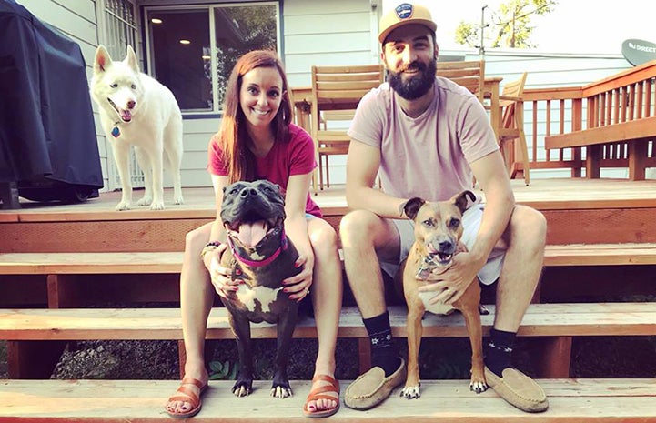 Ashley and Travis Tzioumis with three dogs sitting on the deck of a home