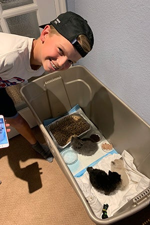 Lucas smiling and looking down into a tub holding foster kittens