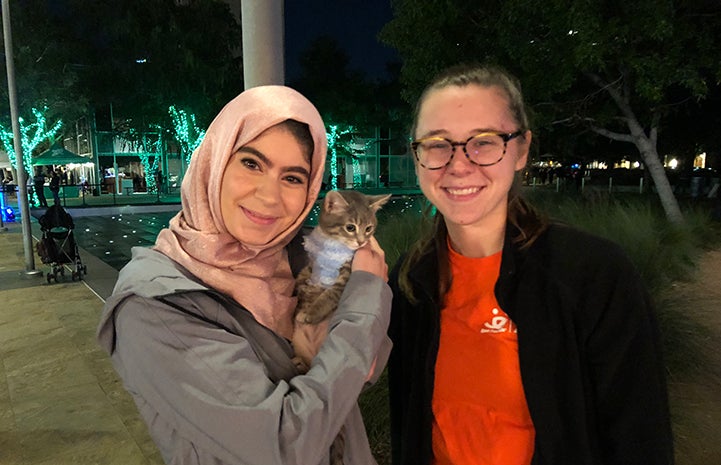 Small kitten being adopted by a woman standing next to someone else from Best Friends