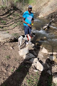 Man standing next to Comet the dog outside next to a river