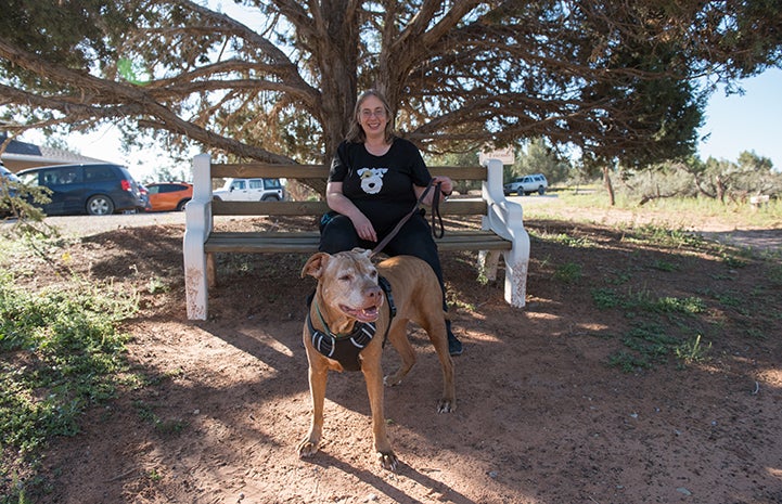 Adopter Caroline Lynch sitting on a bench behind DoSiDo the dog