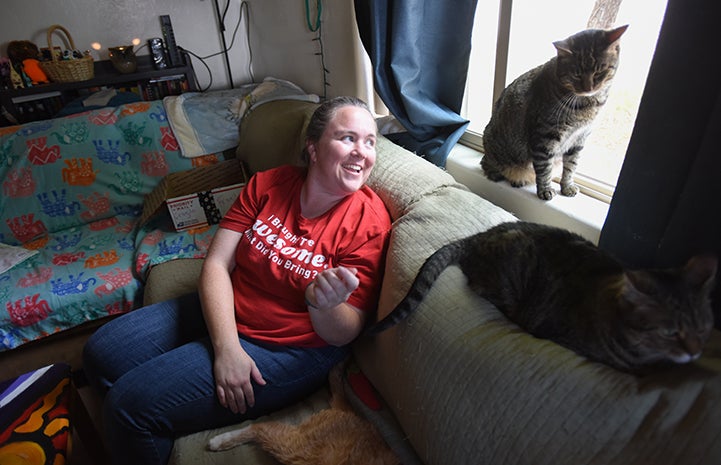 Heather sitting on the couch looking at her two brown tabby cats, RJ and Koda