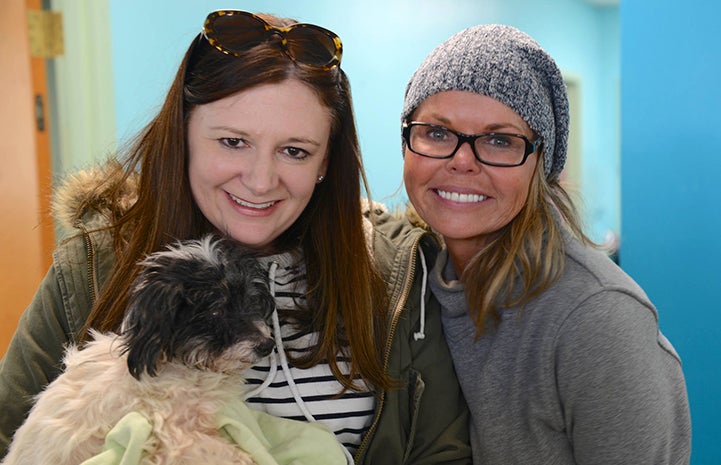 Two women posing with a small, fluffy black and white dog