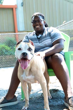 Donovan Dodds sitting on a chair outside with a pit bull terrier in front of her who she's petting