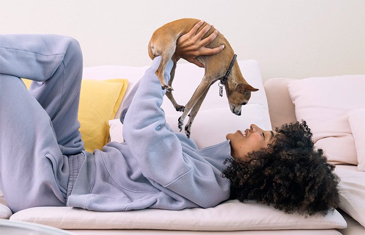 Mueni Rudd lying on a couch holding a puppy up and smiling