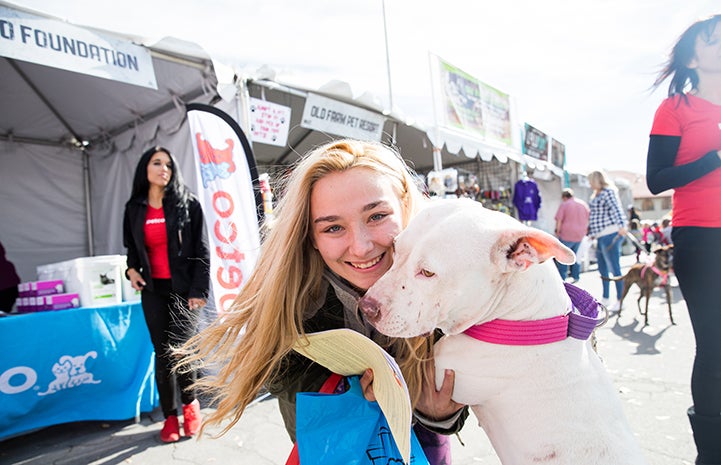 White pit-bull-type dog being adopted by a woman at the NKLA Super Adoption event