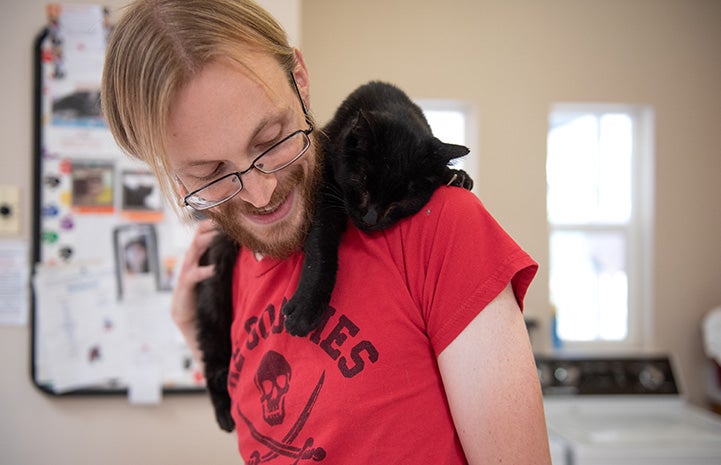 Black cat draped over the shoulder of male caregiver