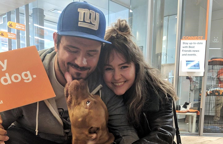 Man and woman holding Carmine the dog he is giving a kiss to the man