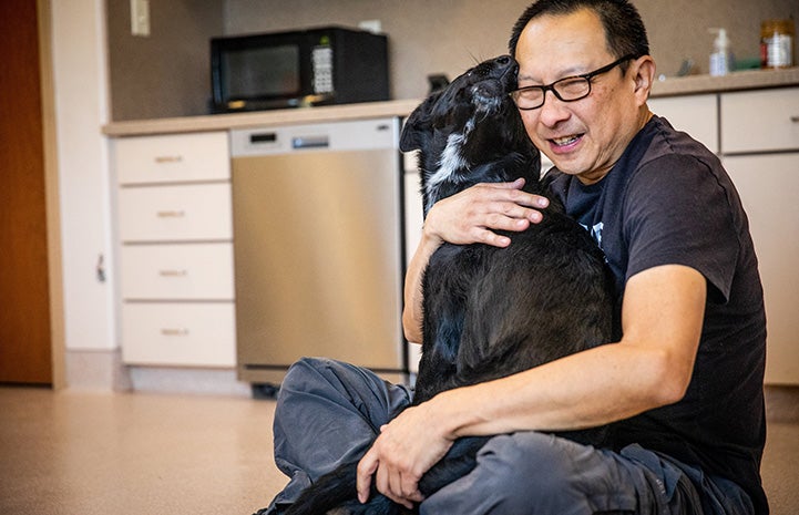 Dogtown caregiver Steven sitting on the ground hugging a big black and white puppy