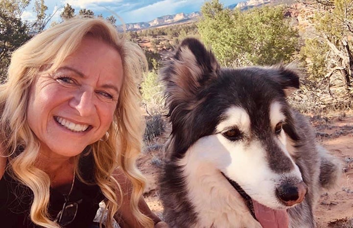 Melanie Marks with Gary the dog with trees and blue sky in the background