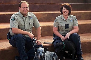 Dog sitting with a man and Bailee Mabe, both in uniform