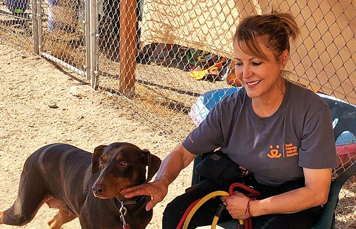 Woman wearing a Best Friends T-shirt sitting next to Hannah the Doberman