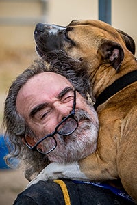 Volunteer Layne Dicker holding a brown dog with his glasses slightly knocked off