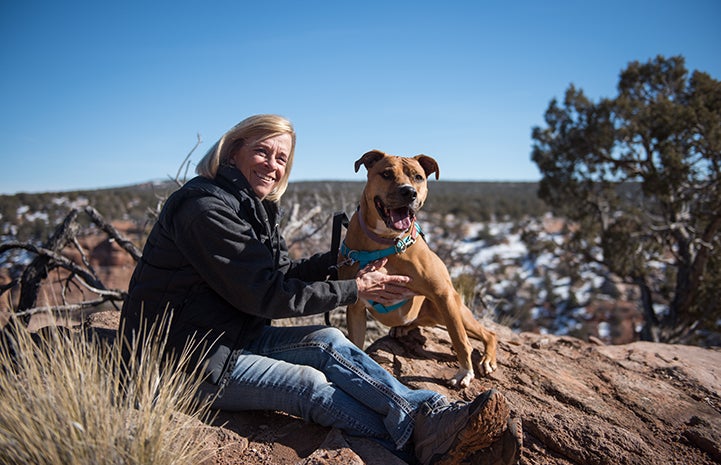 Volunteer Denny Erardi sitting on a rock outcropping with Harvey the dog