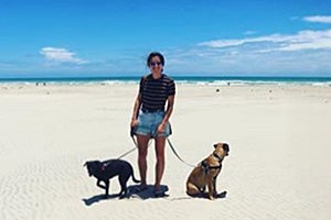 Volunteer Chelsea Hughes with two dogs on leashes on a beach