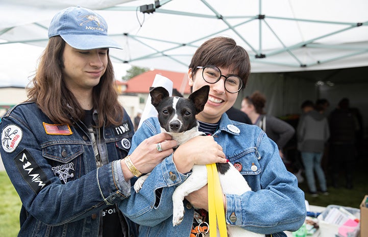 Two smiling people holding a small black and white dog