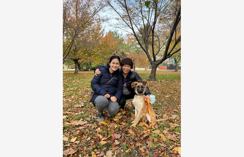 Two people posing with Pickle the puppy in a park