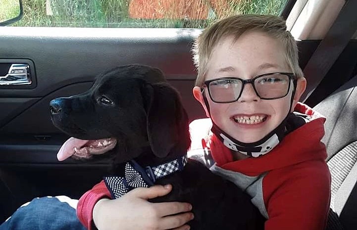 Bryson Kliemann sitting in a car hugging Bruce the puppy