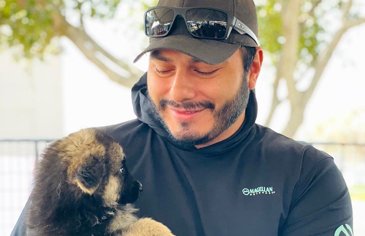 Person wearing a hat looking down lovingly at a puppy