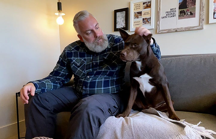 Scott sitting on a couch with Piney the dog