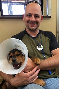 Daniel snuggling a puppy wearing a cone