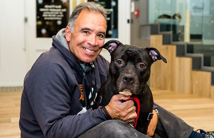 Smiling man sitting on the floor with a black pit-bull-terrier-type dog