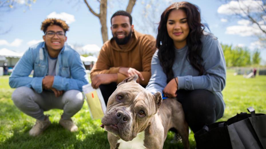 Three smiling people outside in the grass with a big dog