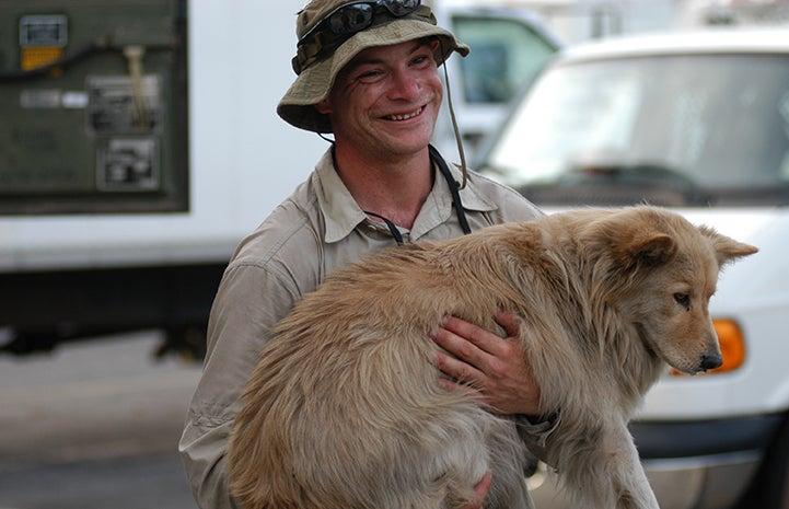 person carrying a tan dog after rescuing him following a hurricane