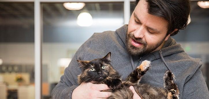 Man cradling a tortoiseshell colored cat in his arms