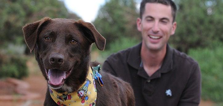 brown dog smiling next to dog trainer