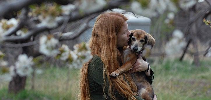 Woman holding small dog and kissing the dog on the cheek