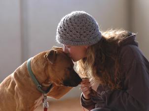 Best Friends employee Carissa kissing the top of Oscar's head, who is one of the Vicktory dogs