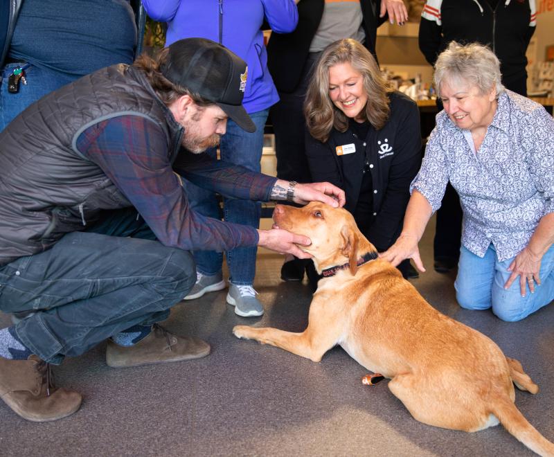 Smiling people petting a happy dog laying down on the floor