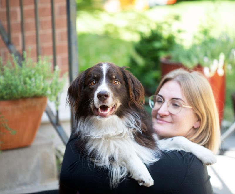 Smiling person outside with a brown and white dog whose paws are over her shoulder