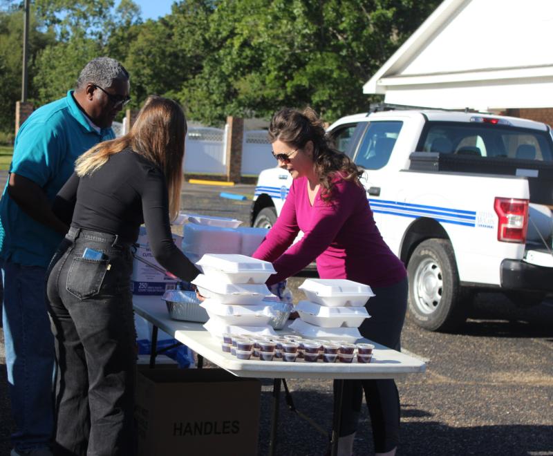 People next to a table full of styrofoam containers containing food from the Pancakes and Puppies fundraiser