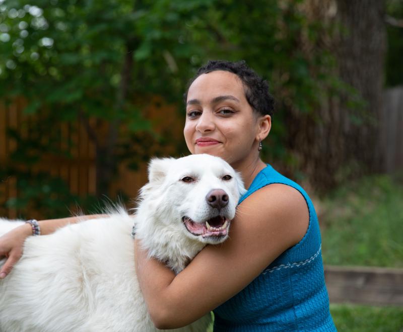 Smiling person hugging a large white dog outside in a fenced area