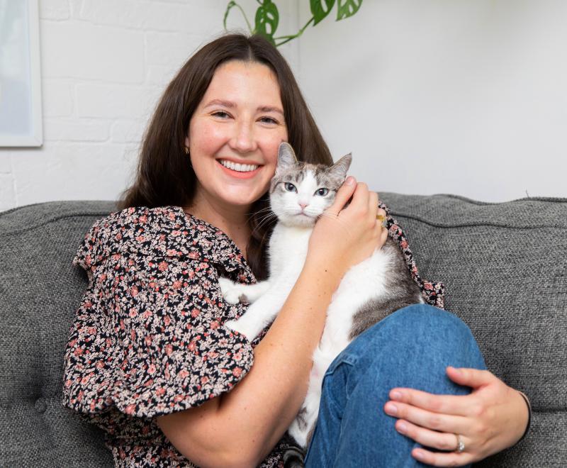 Smiling person holding a cat while sitting on a couch