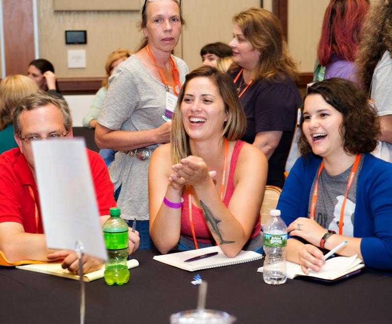 Smiling people sitting around a table with paper and pens in front of them on the table