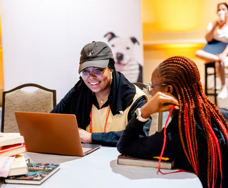 Two people sitting at a table looking at a laptop in front of them