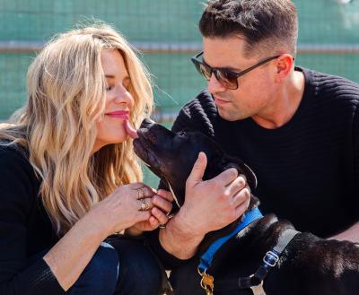 Two smiling people playing with a dog 