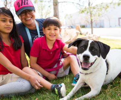 Family of three outside on the grass with their black and white dog