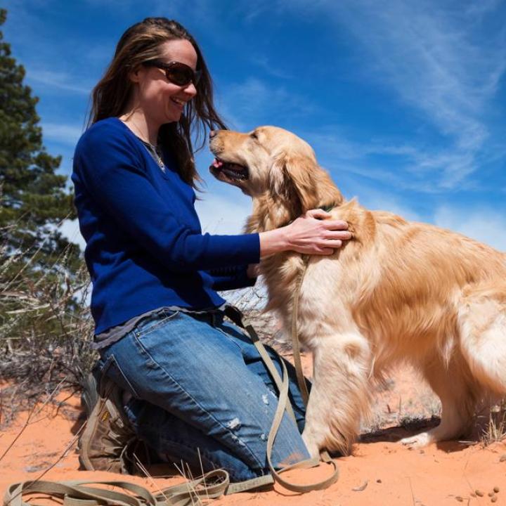 Person kneeling with dog in red sand surrounded by desert brush and blue sky