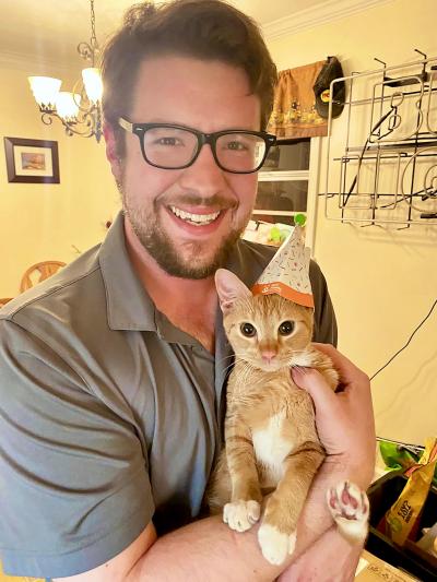 Smiling person holding Spud the kitten who is wearing a celebratory hat