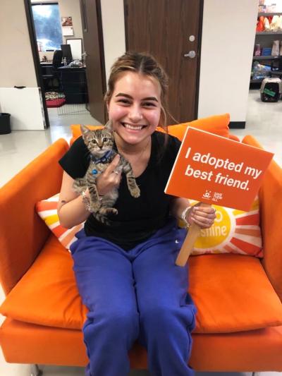 Smiling person holding Eli the kitten and a sign that says, I adopted my best friend